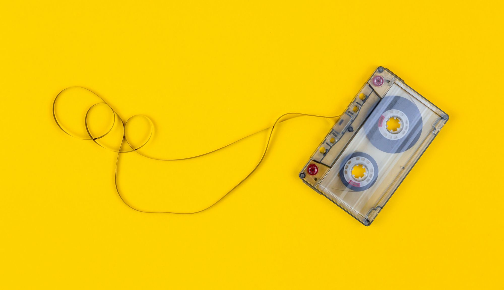 A cassette tape on a yellow background with some of its tape pulled out and looped around.