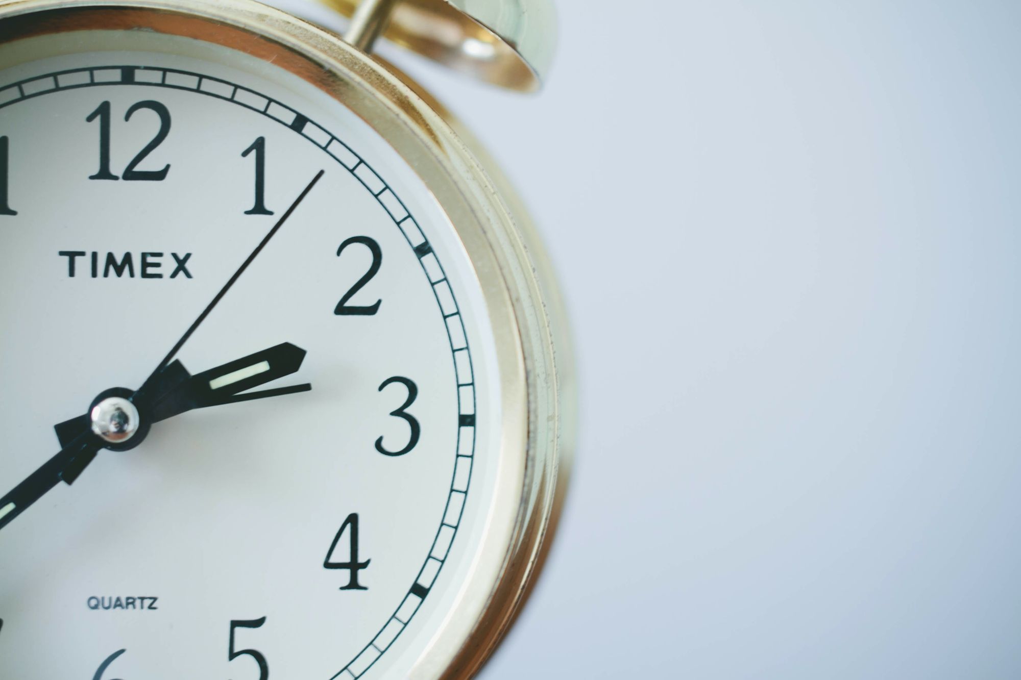 A close up of a gold alarm clock, offset from the center. It is two-something; you can't see the minute hand.