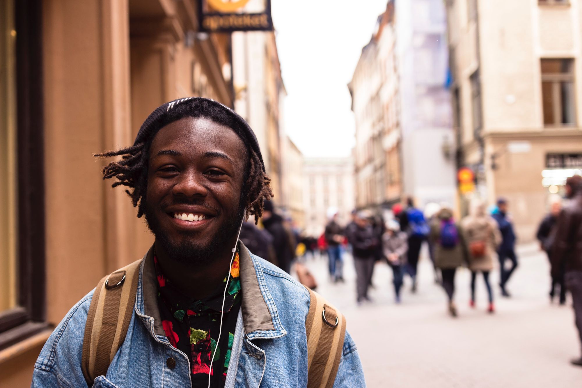 A Black man wearing headphones and smiling while walking in a city.