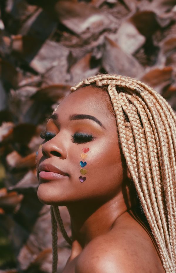 Serene Black femme with blonde dreads in the sun with heart stickers in rainbow colors down her cheek