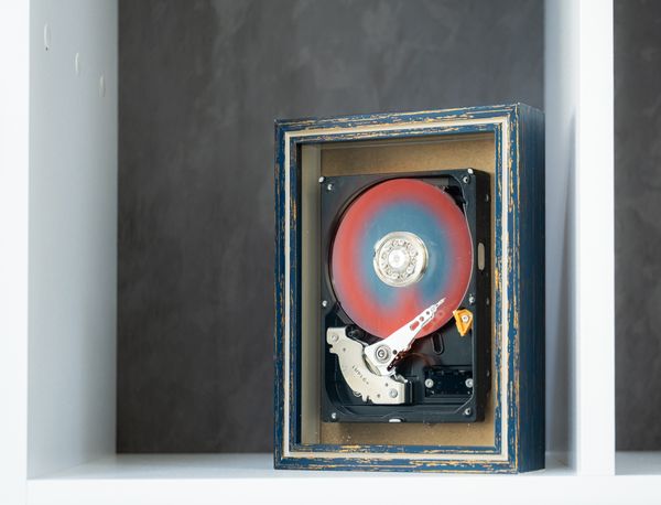 A decayed analog hard disk drive displayed inside a weathered shadowbox.