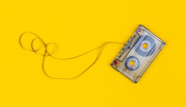A cassette tape on a yellow background with some of its tape pulled out and looped around.