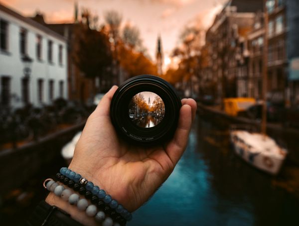 A hand holding a camera scope. The blurry cityscape around is of Venice; the lens focuses in on the center.
