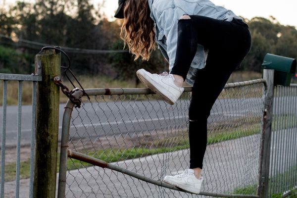 Someone in a jean jacket, sneakers, and leggings climbing over a locked and chained fenc
